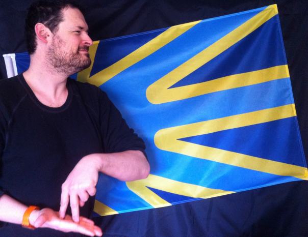 Arnaud Balard, signing STAND, with the Deaf Union flag
